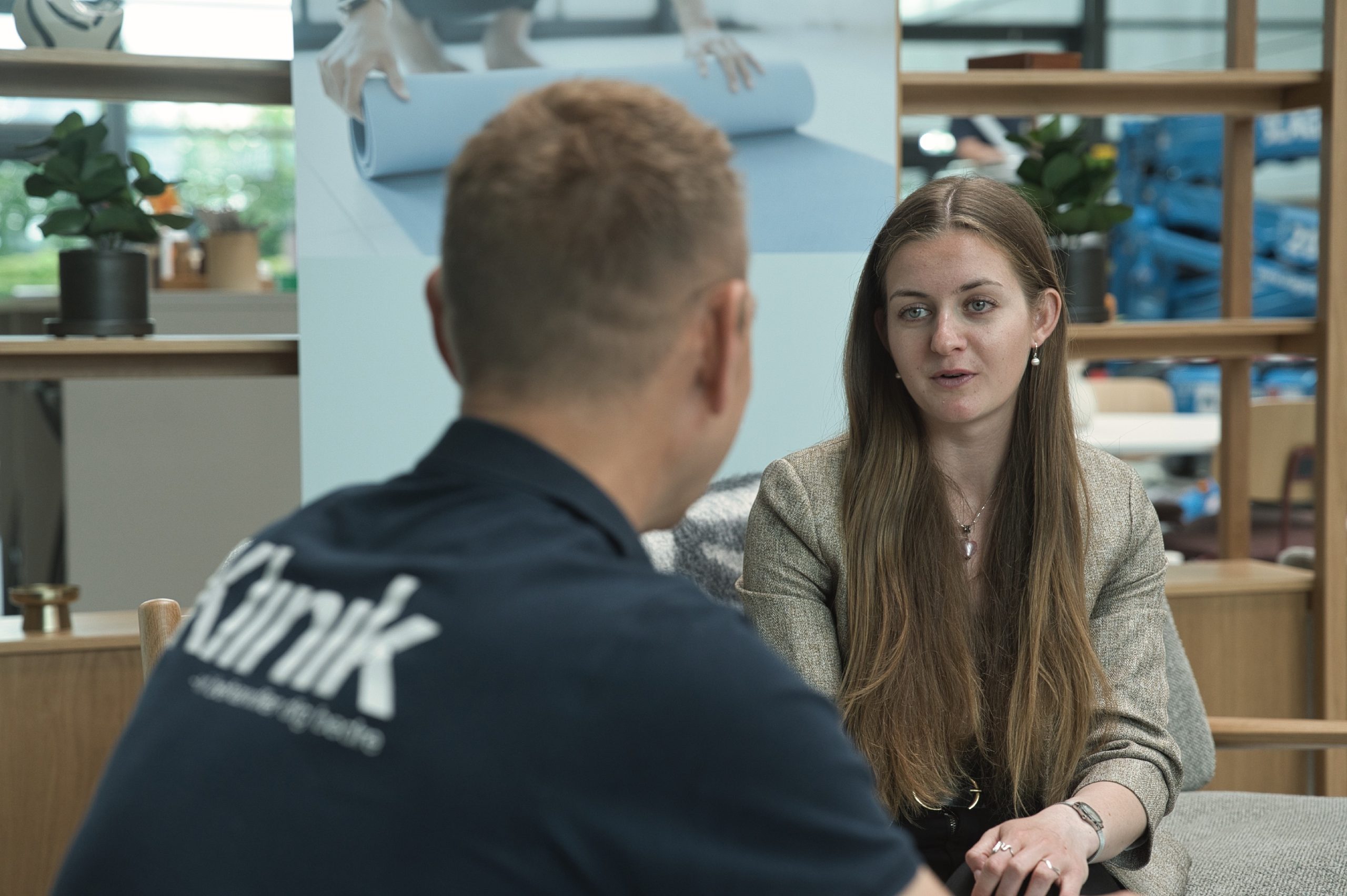 Behandler med Klinik-logo på ryggen lytter, mens kvinden i jakke taler