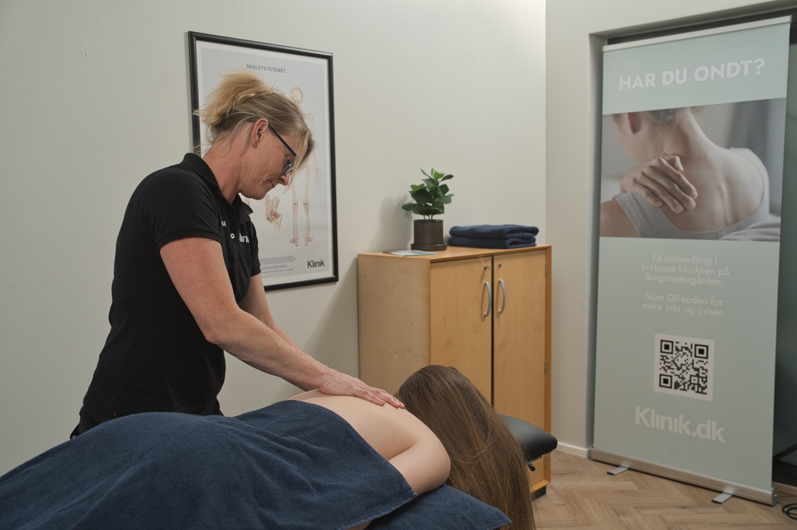 Kvindelig behandler i sort polo masserer en patients ryg på en briks