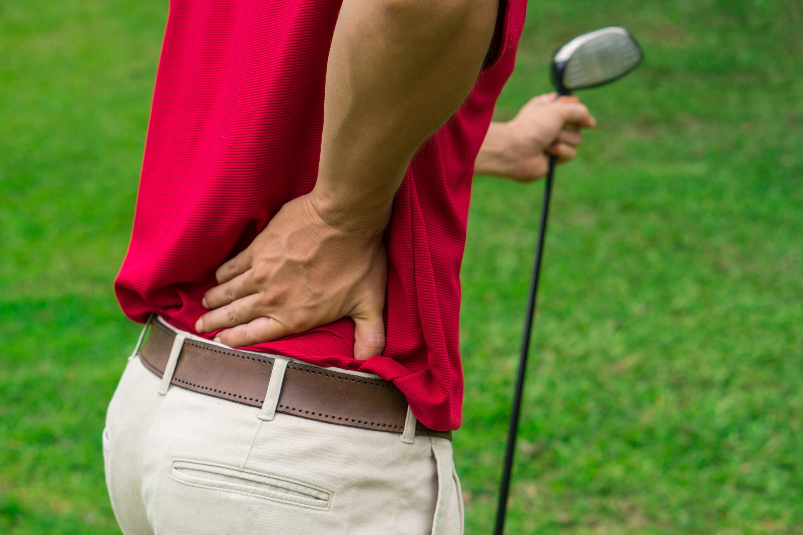 Golfspiller i rød polo holder sig på lænden med golfkølle i hånden