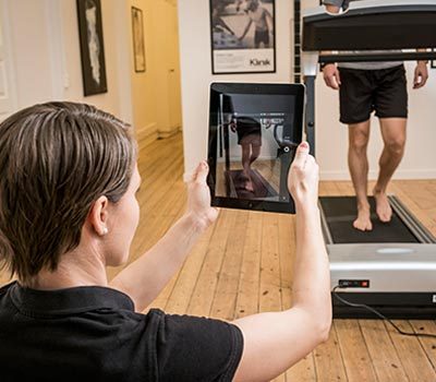 Kvinde holder tablet med løbeanalyse foran en mand på løbebånd